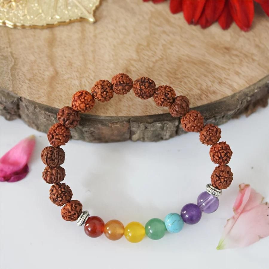 Bracelet with brown rudraksha beads and colorful gemstones on a wooden surface with flowers.