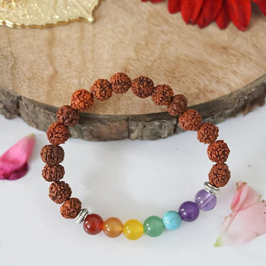 Bracelet with brown rudraksha beads and colorful gemstones on a wooden surface with flowers.